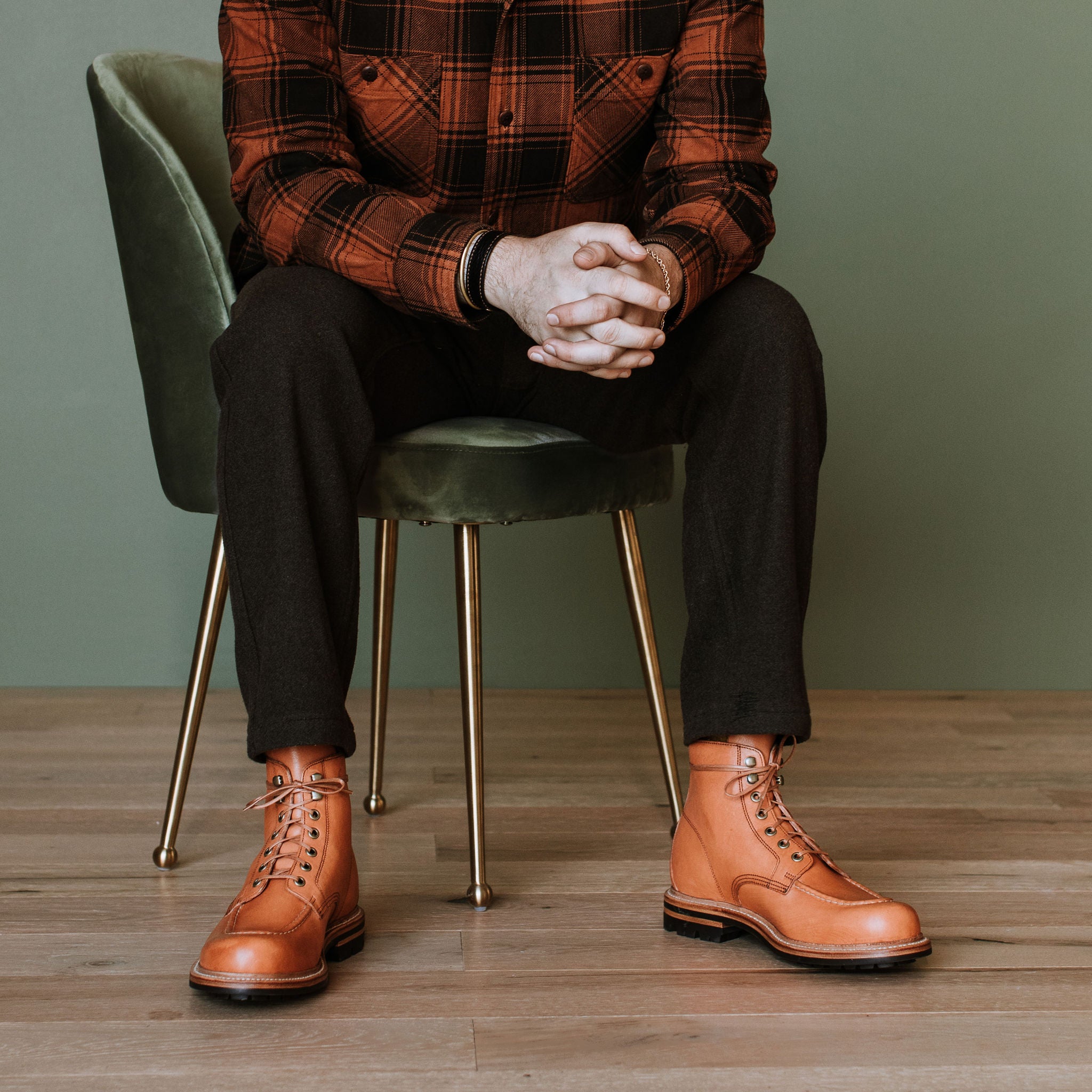 Person wearing brown leather boots sitting on a green chair against a green wall.